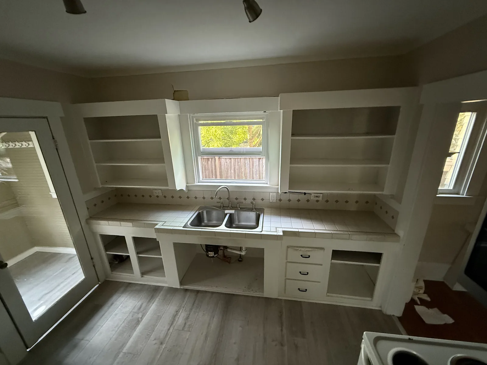 Kitchen cabinet run with the doors off and the boxes emptied, the window over the sink in place