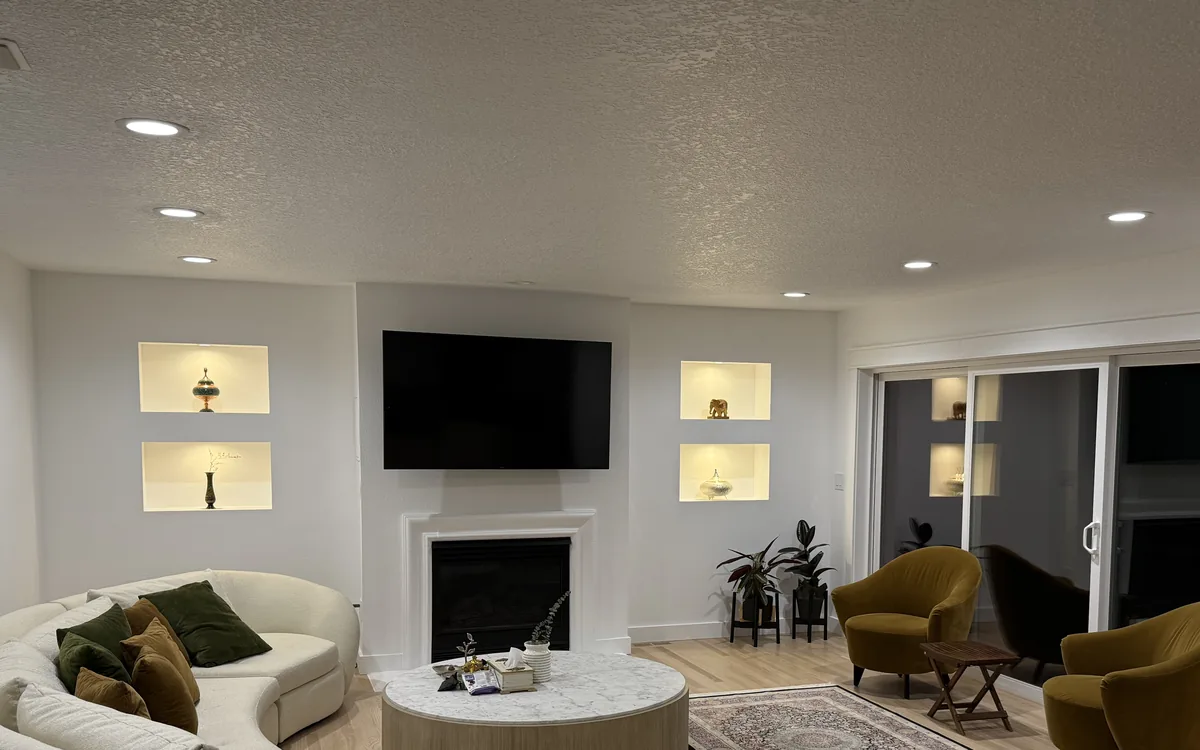 The same living room after remodel: wide plank flooring, lit display niches in the wall and recessed ceiling lights