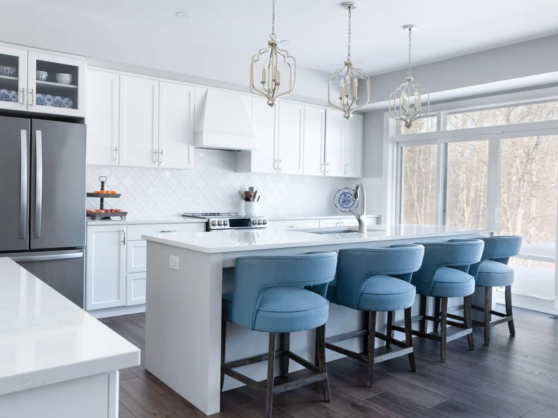 White kitchen with a blue island, pendants and wood floors