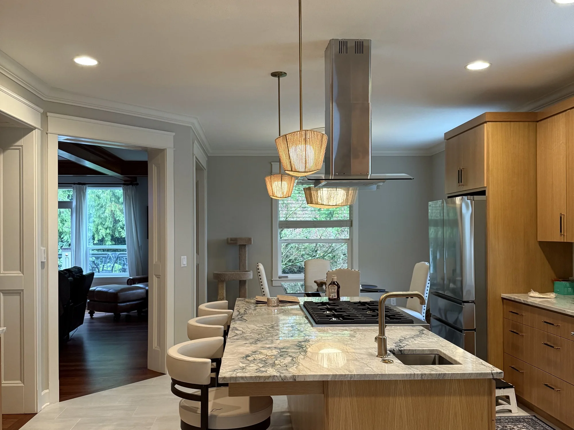 A remodeled kitchen island with a gas cooktop, a stainless sink and a veined stone counter, with a wide cased opening to the living room on the left