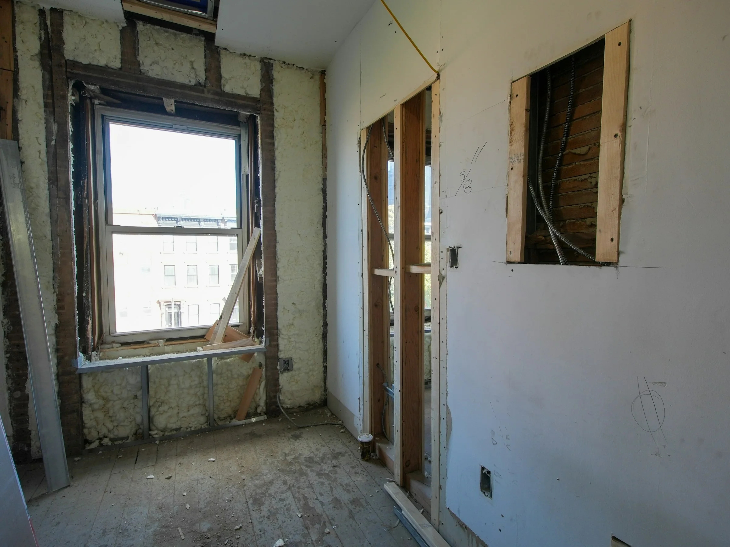 Room under renovation with a wall opened to the studs beside a window
