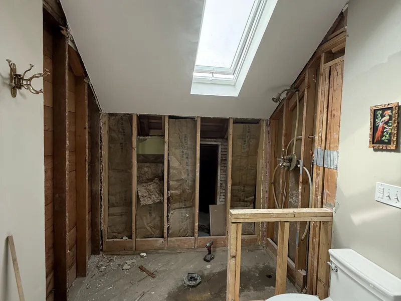 Bathroom stripped back to the studs during a remodel, with the skylight opening framed and the supply lines capped