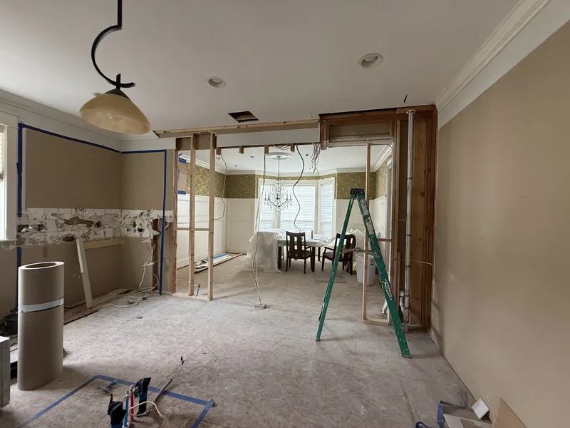 Interior stripped to bare walls mid remodel, with a new opening framed through to the dining room and a temporary post in place