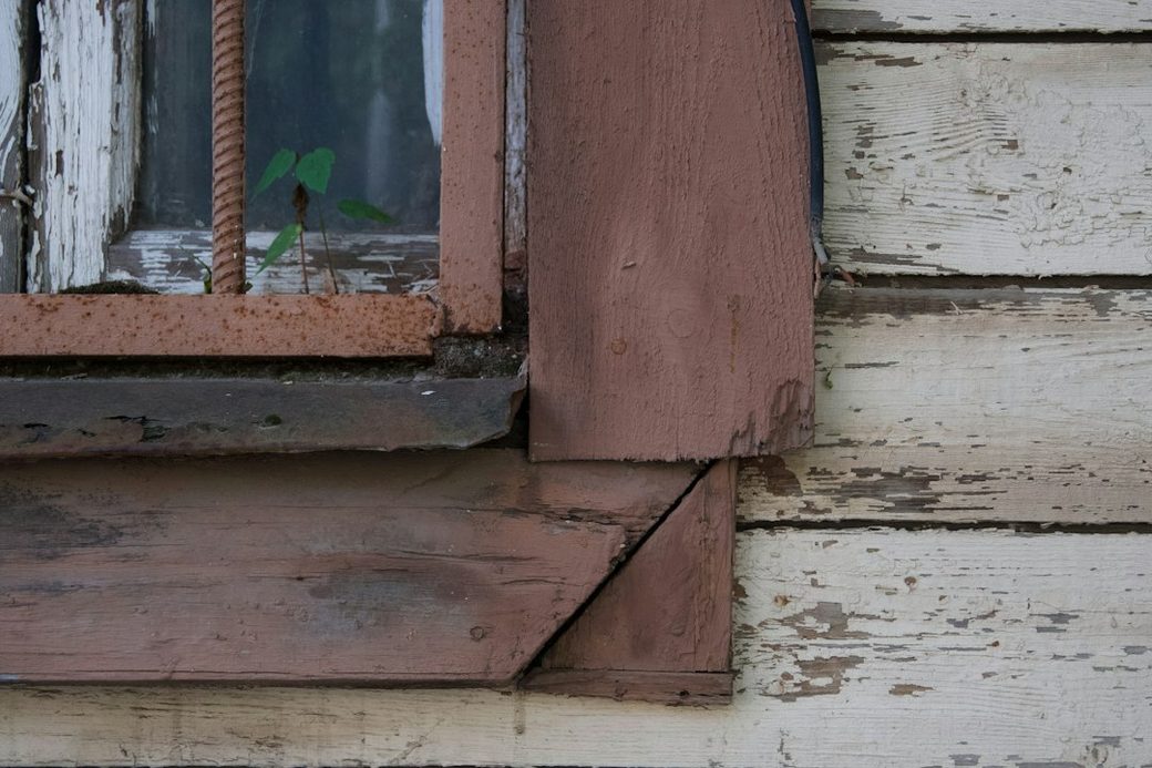 Closeup of peeling paint and weathered wood siding at a window