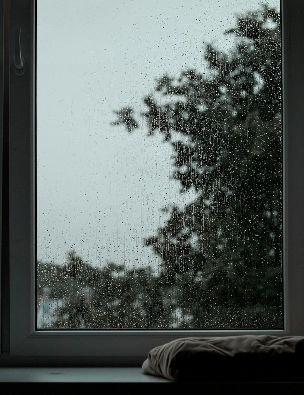 Rain streaked window with a tree outside